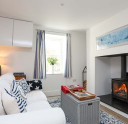 A living room with white sofa and blue cushions next to a window and a fireplace with fire burning at Cwrt Dwyran near Niwbwrch Newborough