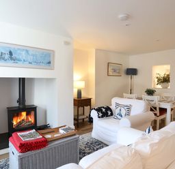 A living room with a wood burning stove a white sofa and armchair a dining table with chairs and framed paintings on the walls at Cwrt in Dwyran near Niwbwrch Newborough