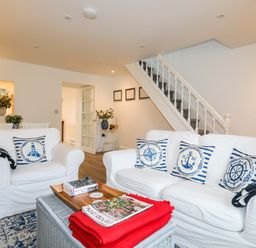 A living room with white sofas and nautical pillows near a staircase at Cwrt in Dwyran near Niwbwrch Newborough