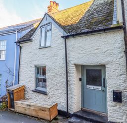 Exterior view of a white textured cottage with a blue door labeled Alpha Cottage in Dittisham near Dartmouth