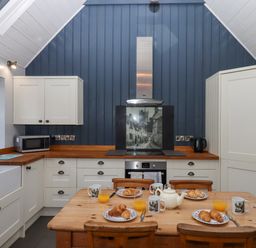 A kitchen with wooden table and chairs set with mugs croissants and glasses of orange juice at Alpha Cottage in Dittisham near Dartmouth