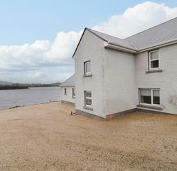 A gravel area next to a white house by a body of water with cloudy sky at Dock at Dominic's Ballyheerin near Downings