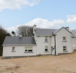 A white two story house with multiple windows and a gray roof on a gravel area surrounded by trees at Dock at Dominic's Ballyheerin near Downings
