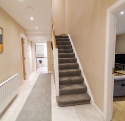 A hallway with carpeted stairs and a gray runner rug next to a living room with a television and wooden coffee table at Dock at Dominic's in Ballyheerin near Downings