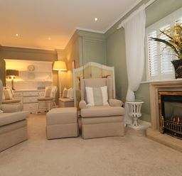 A living room with beige armchairs and ottomans a fireplace with flowers on the mantel and a white cabinet with chairs at Tree Tops in Broadway