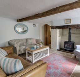 A living room with two sofas a coffee table a wood burning stove and a purple armchair at Amy Cottage in West Lulworth