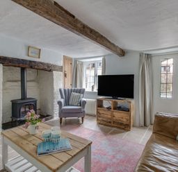 A living room with a wood stove fireplace a wooden coffee table a gray armchair and a leather sofa at Amy Cottage in West Lulworth