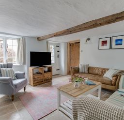 A living room with a brown leather sofa a blue armchair a striped sofa a wooden coffee table a television on a wooden stand and exposed wooden beams at Amy Cottage in West Lulworth