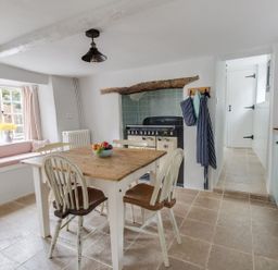 A kitchen with wooden table and chairs fruit bowl stove and window seat at Amy Cottage in West Lulworth