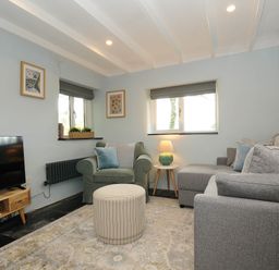 A living room with a gray sofa a green armchair a round ottoman and a wooden TV stand at Rose Cottage in Callington