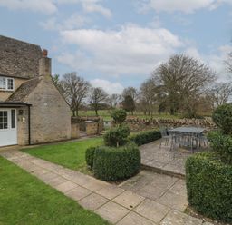 A garden patio with outdoor dining table and chairs next to a stone cottage at Stable Cottage in Lechlade-On-Thames