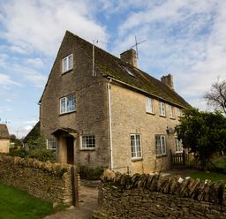 A stone house with multiple windows and a stone wall in front at Stable Cottage in Lechlade-On-Thames