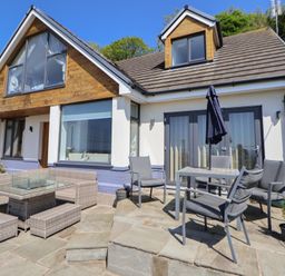 An outdoor patio area with chairs tables and umbrella outside a house with large windows at Buzzards View in Dyserth