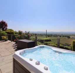 An outdoor patio with a hot tub a storage box and flower bushes overlooking fields and hills at Buzzards View in Dyserth