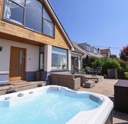 An outdoor patio with a hot tub chairs tables and plants outside a modern house at Buzzards View in Dyserth