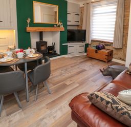 A living room with a dining table set for breakfast a wood stove a television and a leather sofa at Number Ten in Amble