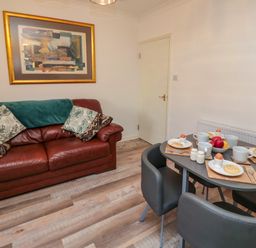 A dining area with a table set for four and a leather sofa with cushions and a framed artwork on the wall at Number Ten in Amble