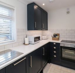 A kitchen with black cabinets a white countertop a microwave toaster oven and window blinds at Number Ten in Amble