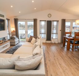 A living room with a sectional sofa a fireplace a wall-mounted TV and a dining table with chairs at 12A Lake Escape in Carnforth