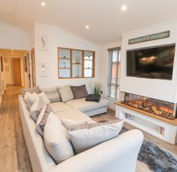 A living room with a large sectional sofa a wall-mounted television and an electric fireplace at 12A Lake Escape in Carnforth