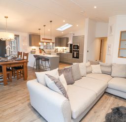 An open plan living room kitchen and dining area with a large beige sectional sofa wooden dining table with chairs and a kitchen island with stools at 12A Lake Escape in Carnforth
