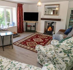 A living room with floral armchairs a gray sofa a red patterned rug a wood-burning stove and a bookshelf at Chapel Hill House Chapel Hill near Pembroke