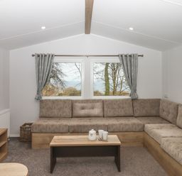 A living room with an L shaped sofa a wooden coffee table a television and windows with curtains at 5 Manor Park in Bucks Cross Bideford