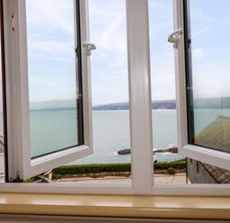 A view through an open window overlooking the sea with a distant coastline and buildings at Blue Horizon in Port Isaac