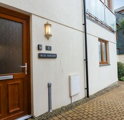 The exterior entrance of a unit with a wooden door window and signs for number 5 and Blue Horizon an outdoor path and foliage at Blue Horizon Port Isaac