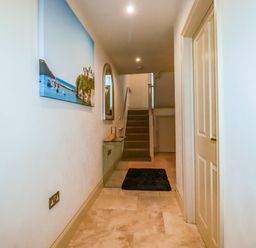 A hallway with stairs at the end a glass table a mirror and a painting on the wall at Blue Horizon in Port Isaac