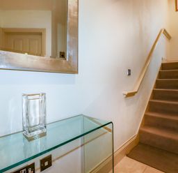 A staircase with carpeted steps and a railing next to a wall with a large mirror and a glass table holding a glass vase at Blue Horizon in Port Isaac