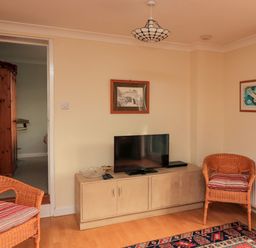 A living room with a television on a cabinet two wicker chairs with cushions and framed pictures on the walls at Garden View in Hillhead near Brixham