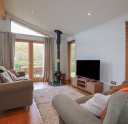 A living room with sofas a television a wood stove and large windows at 3 Hedgerows in Lanreath