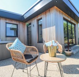 An outdoor patio with two wicker chairs a round table with a champagne bucket and a wooden house exterior at Little Victory in Pendeen