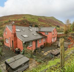 A large red house with multiple chimneys and skylights surrounded by a stone wall and hillside at Ysgubor in Dinas Mawddwy near Dolgellau
