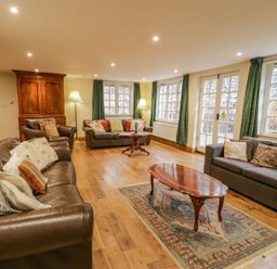 A living room with leather and fabric sofas wooden coffee tables a wooden cabinet and green curtains at Ysgubor in Dinas Mawddwy near Dolgellau