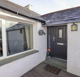 An entrance door with a doormat and flowers next to it and a window on the left at Lakeland View Lodge in Keswick