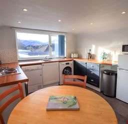 A kitchen with a round wooden table and chairs a window over the sink appliances including a dishwasher washing machine microwave and fridge at Lakeland View Lodge in Keswick
