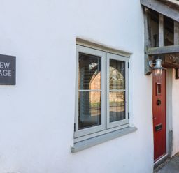 The exterior of a white cottage with a red door a window and a sign that says Curlew Cottage at Curlew Cottage in North Curry near Taunton