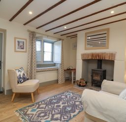 A living room with a stove fireplace wooden beams on ceiling and a patterned rug at Curlew Cottage North Curry near Taunton