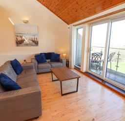 A living room with two grey sofas, wooden coffee table, wall painting, clock, and glass sliding door at Waters Edge in Embleton