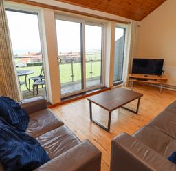 A living room with two leather sofas a wooden coffee table a TV on a stand and sliding glass doors leading to a balcony at Waters Edge in Embleton