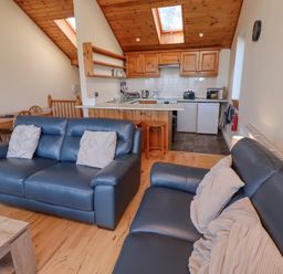 A living room with blue sofas and a kitchen with wooden cabinets and skylights at Dunstanburgh View in Embleton