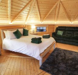 A bedroom with a double bed, green pillows, folded towels, a dark sofa, rug, and wooden walls at The Hideaway in Dungiven Londonderry