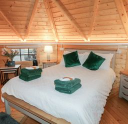 A bedroom with a large bed with white bedding and green pillows inside a wooden cabin at The Hideaway in Dungiven Londonderry