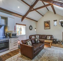 A living room with leather sofas and wood stove next to a kitchen area at Upper Calffield Barn in Camrose near Haverfordwest