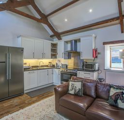 A kitchen with white cabinets stainless steel appliances and a brown leather sofa with horse pillows at Upper Calffield Barn Camrose near Haverfordwest
