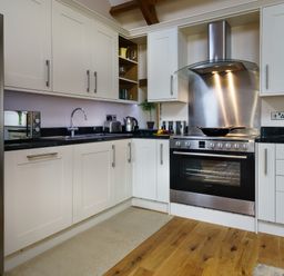 A kitchen with white cabinets stainless steel appliances wooden floor and black countertops at Upper Calffield Barn in Camrose near Haverfordwest