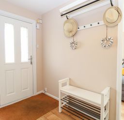 An entryway with a white door a white bench with black metal shoe racks a wall-mounted coat rack with two hats and two heart-shaped decorations a gray sofa visible in the adjacent room at White Lion Retreat in Cromer