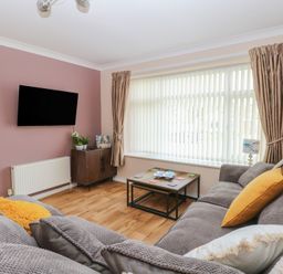 A living room with a grey sofa yellow cushions coffee table and TV on a pink wall at White Lion Retreat in Cromer
